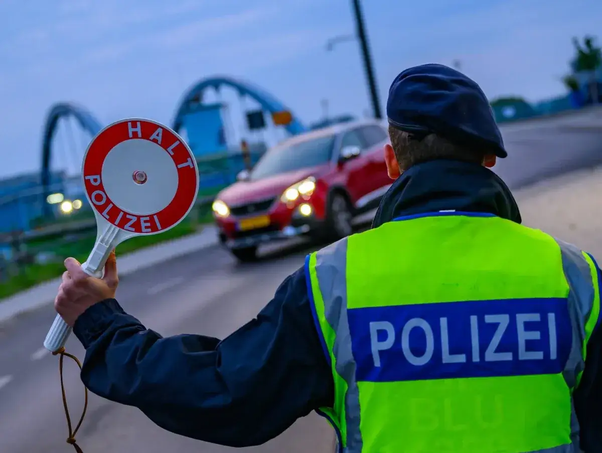 Policjant w kamizelce odblaskowej z napisem POLIZEI zatrzymuje czerwony samochód. Czy kierowca wie, ile papierosów do Niemiec można przewieźć?