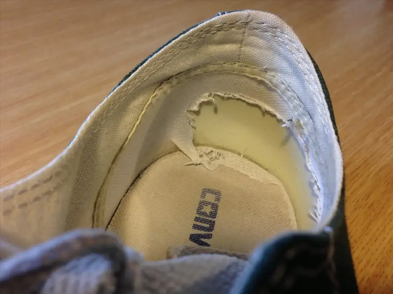 Close-up of the inside of a shoe, showing the lining peeling off near the heel. The sole has a logo.