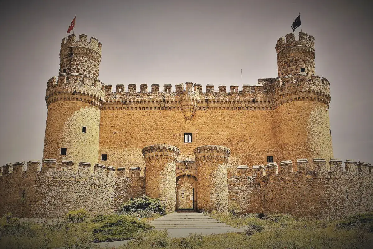 Castillo imponente, uno de los pueblos medievales cerca de Madrid, con torres y murallas de piedra dorada bajo un cielo nublado.