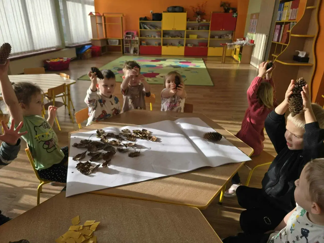 Dzieci w przedszkolu poznają ekologię, bawiąc się szyszkami i liśćmi.