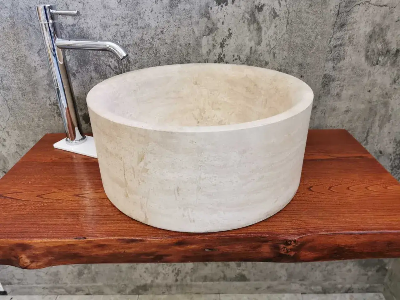 Lavabo cilindrico in pietra naturale, con rubinetto cromato su un piano in legno grezzo. I nomi delle pietre naturali sono un'arte.