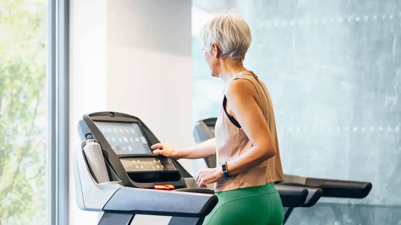 &Auml;ltere Frau stellt die laufband geschwindigkeit ein, um ihr Training zu beginnen.