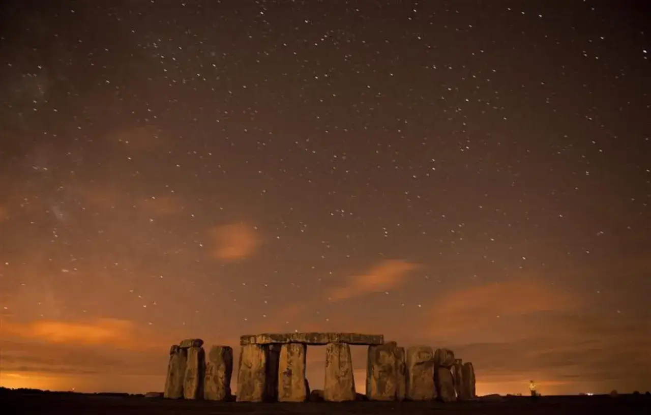 Stonehenge under a starry sky, with faint clouds and the glow of distant lights. Perhaps a wish is being made on one of the many shoot stars.