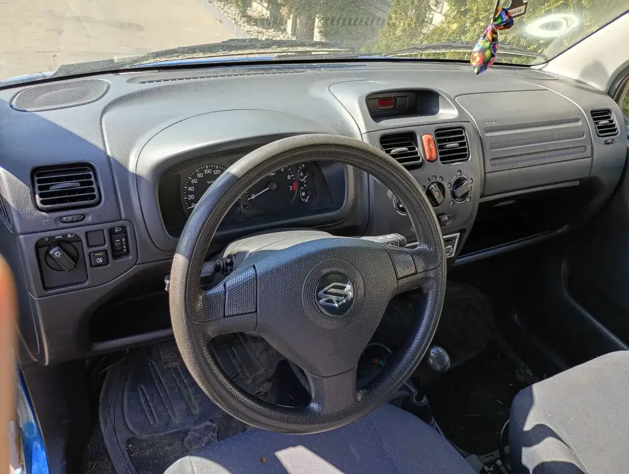 Wnętrze Suzuki Wagon R+. Widok na deskę rozdzielczą, kierownicę z logo Suzuki i siedzenie.