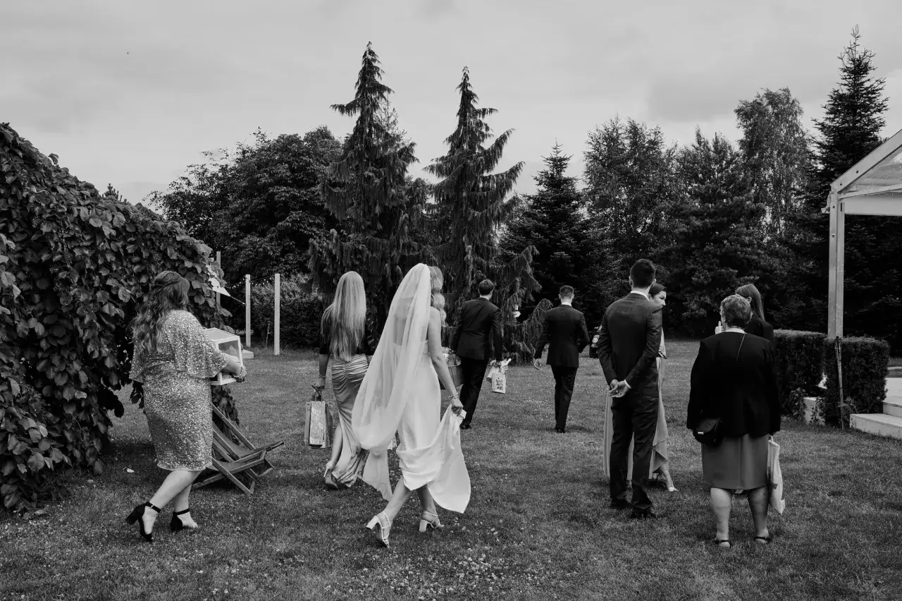 Goście weselni idą przez trawnik, tworząc ciekawy **rytm w fotografii**. Panna młoda w welonie prowadzi grupę.