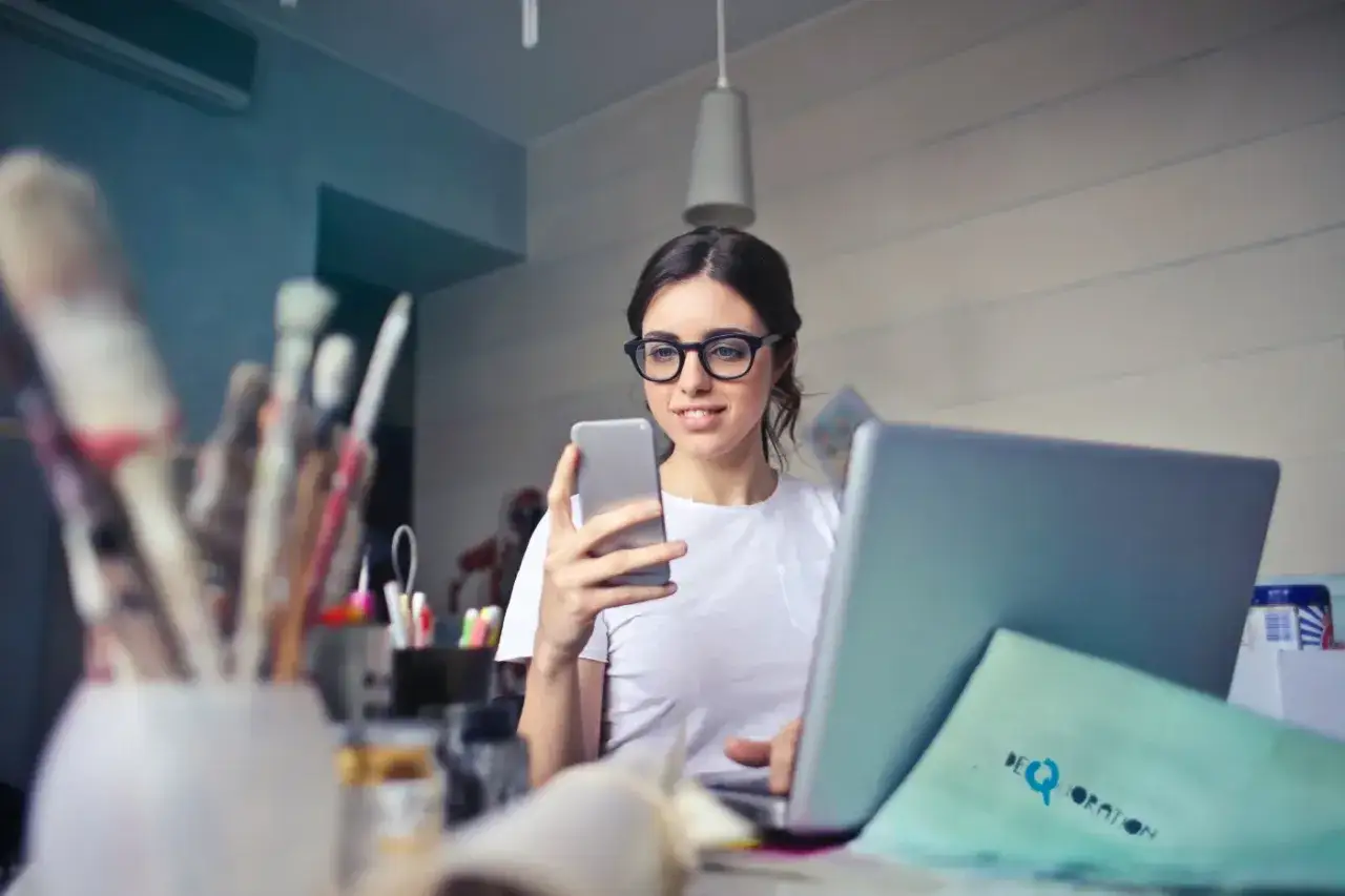 Kobieta w okularach pracuje przy laptopie i telefonie, planując swoją działalność nierejestrowaną.