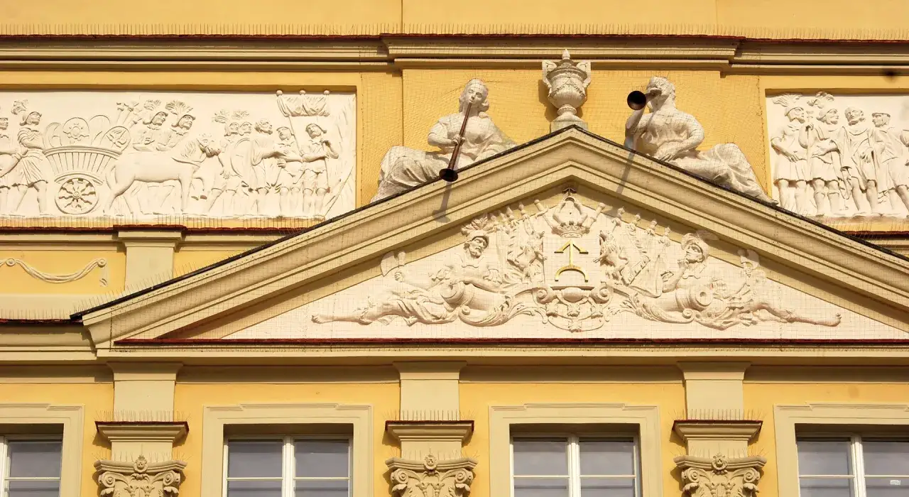 Bogate zdobienia fasady Pałacu Działyńskich w Poznaniu: płaskorzeźby z postaciami i herbem.