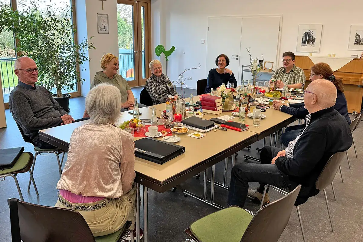 Menschen im Gespräch bei einer Fortbildung zur Seelsorge in NRW. Sie sitzen an einem Tisch mit Büchern und Gebäck.