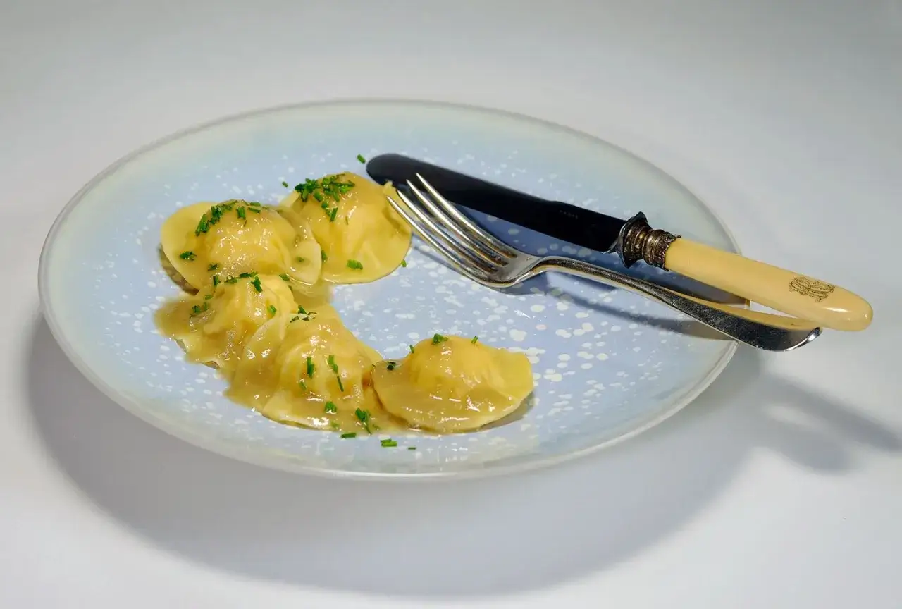 Assiette de ravioli crevette italien, nappés d'une sauce légère et parsemés de ciboulette. Un couteau et une fourchette sont posés sur le plat.