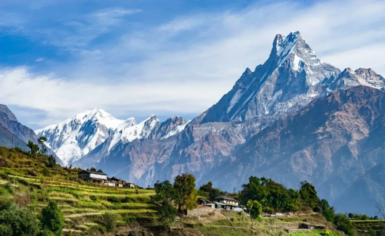 Terrassierte Felder und H&auml;user in Nepal im November, mit schneebedeckten Gipfeln im Hintergrund.
