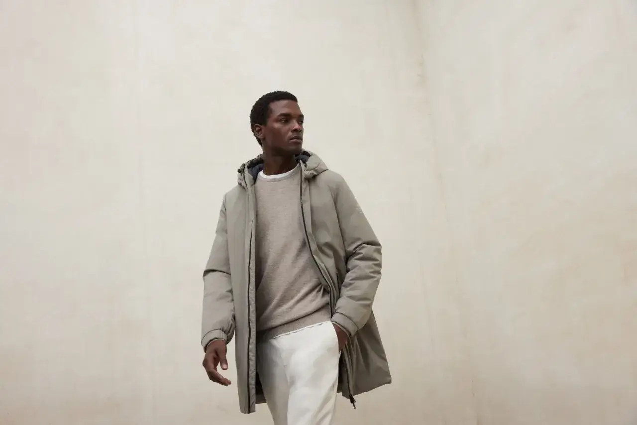 Hombre con outfit urbano: abrigo gris, jersey beige y pantalon beige.
