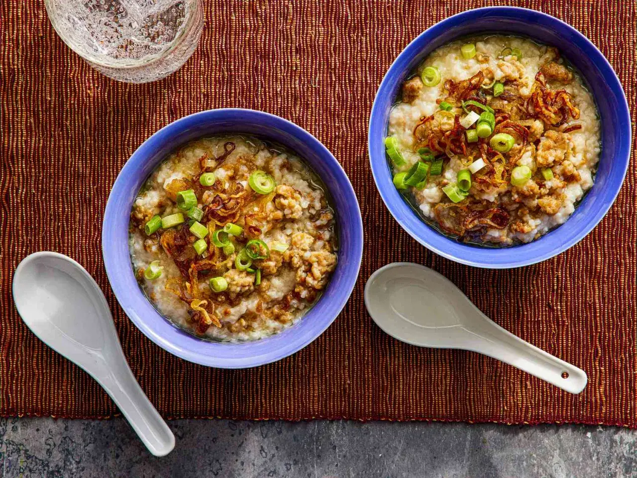 Dwie miseczki aromatycznego congee z mielonym mięsem, posypane szczypiorkiem i chrupiącą cebulką.