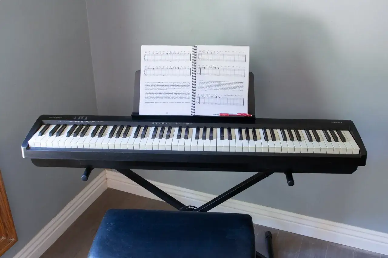 Czarny keyboard Roland FP-10 z nutami na pulpicie, gotowy do grania na pianinie. Obok stoi czarny stołek.