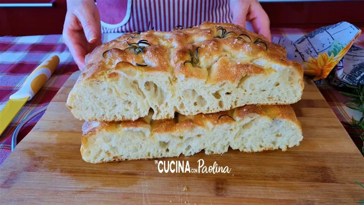 Focaccia alta e soffice, tagliata a metà, con rosmarino e sale grosso, pronta per essere gustata.