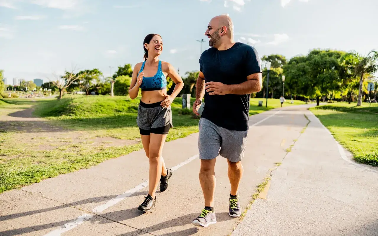 Pareja sonr&iacute;e mientras corre por un parque. El **andar adelgaza** y les ayuda a mantenerse en forma.