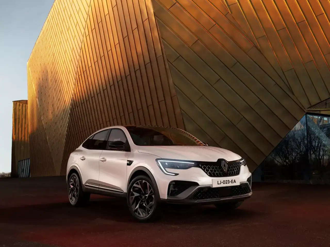 Un bianco SUV coup&eacute; Renault, uno dei nuovi modelli, si staglia contro un edificio moderno con rivestimenti dorati.