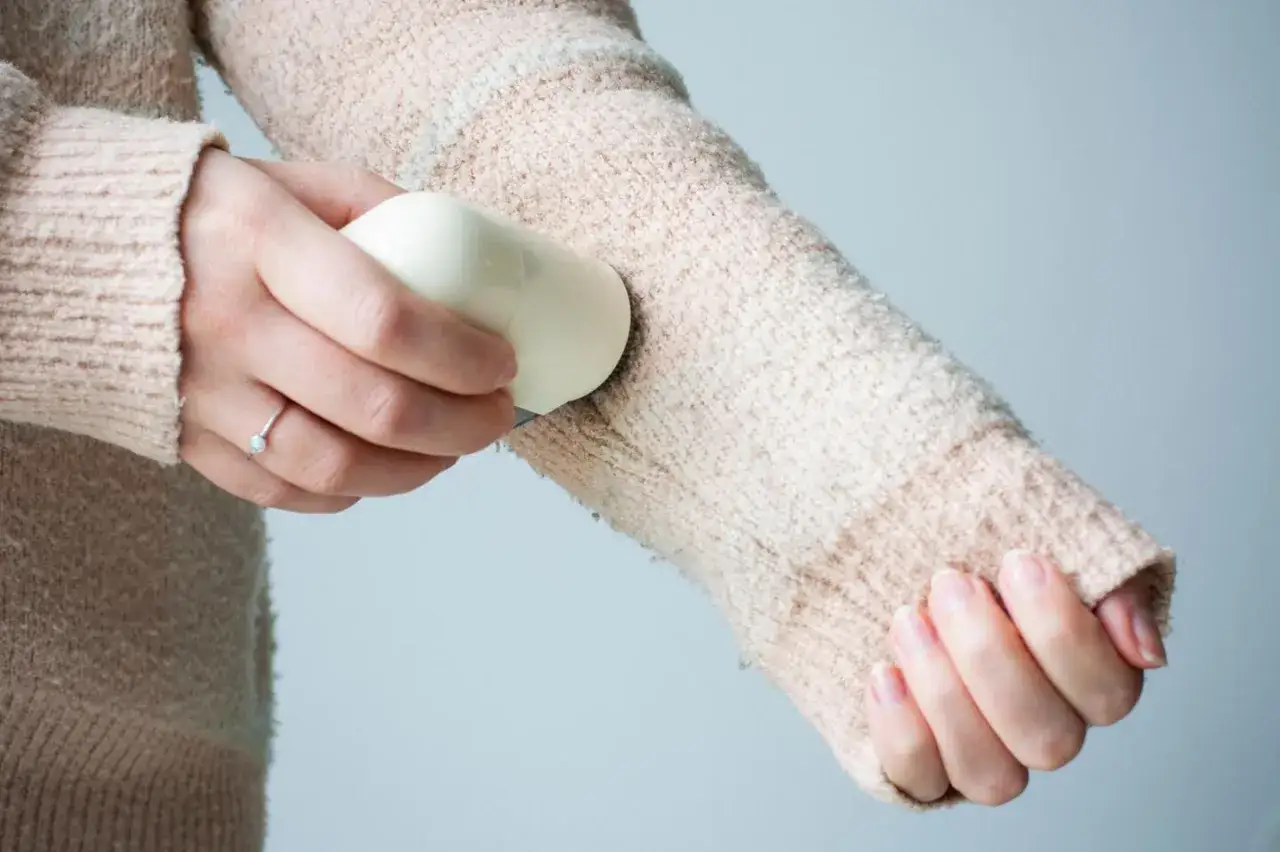 Eine Hand entfernt mit einem Gerät lästige Fusseln, um den Pullover wieder glatt zu machen. Pilling entfernen leicht gemacht.