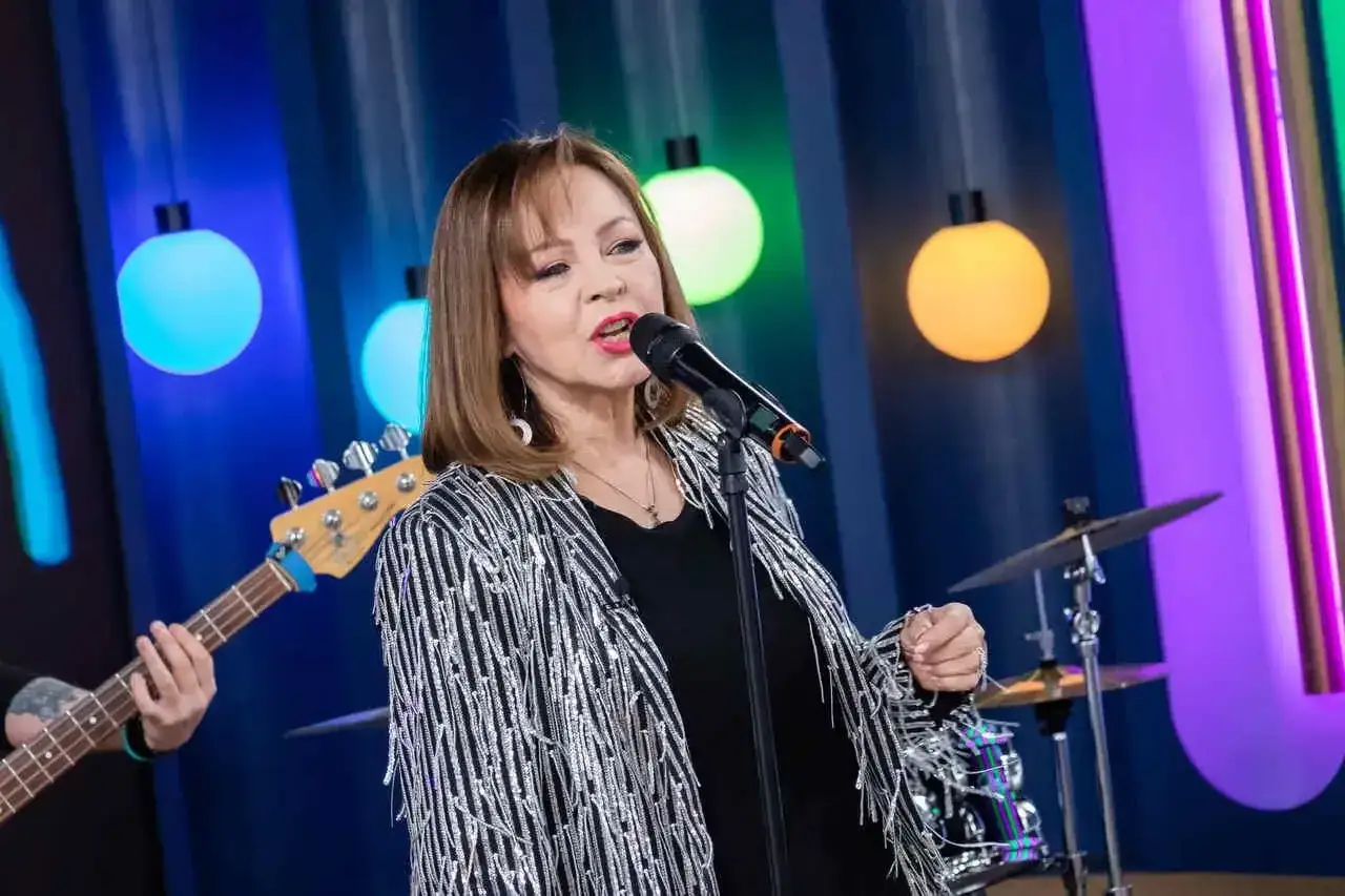 Izabela Trojanowska śpiewa na scenie, w tle kolorowe światła i muzycy. Jej utwory poruszają serca.