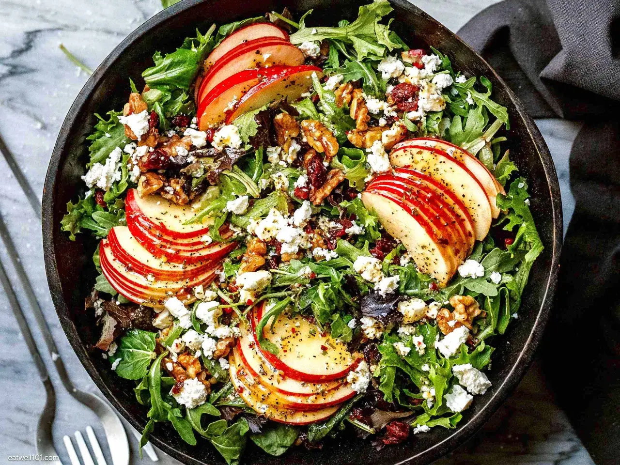 Ein köstlicher Ebly Salat mit Apfelscheiben, Walnüssen, zerbröseltem Käse und getrockneten Cranberries, appetitlich in einer Schüssel serviert.