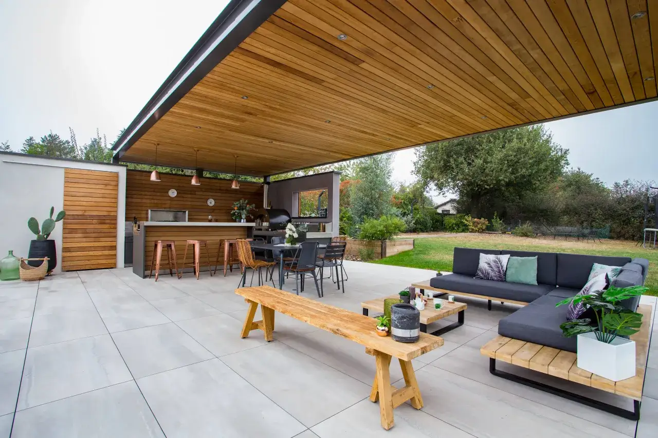 Espace extérieur moderne avec cuisine d'été, coin salon et table à manger, parfait pour un repas d'été entre amis.