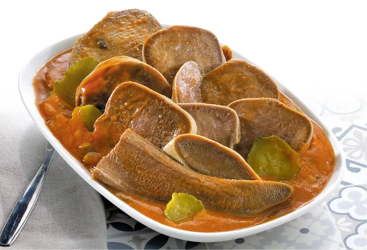 Plat de langue de boeuf en sauce, une recette savoureuse et réconfortante. Les tranches de langue sont tendres et nappées d'une sauce orangée, accompagnées de quelques morceaux de légumes verts.