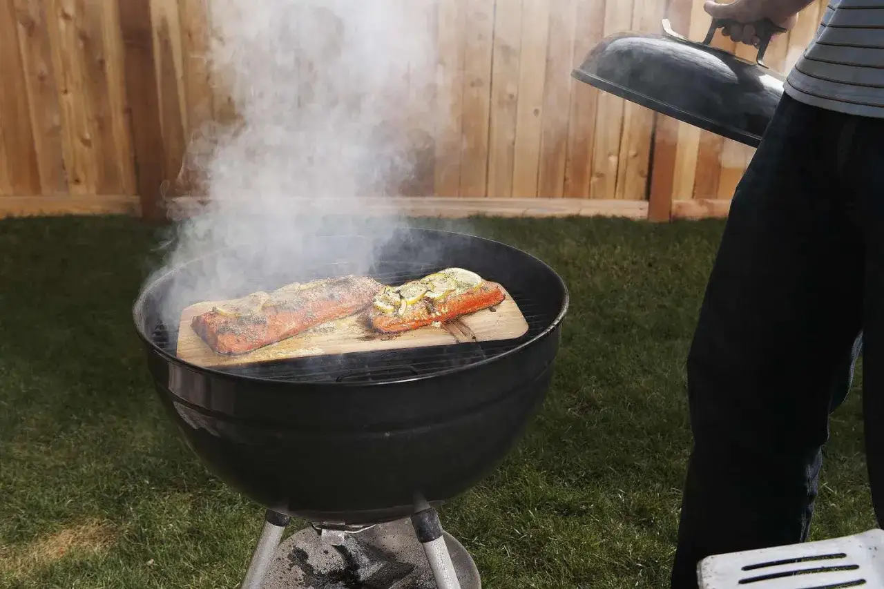 Deux saumons cuisent sur des planches de c&egrave;dre dans un barbecue ouvert, d&eacute;gageant une fum&eacute;e parfum&eacute;e.