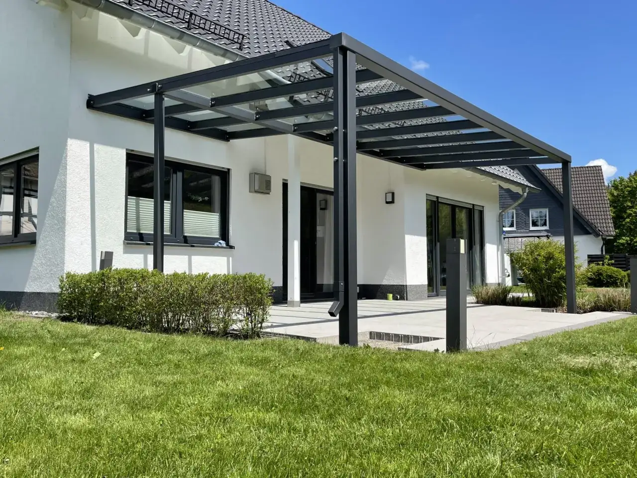 Modernes Terrassendach bauen: Ein elegantes Glasdach mit schwarzer Aluminiumkonstruktion schützt die Terrasse vor Regen.