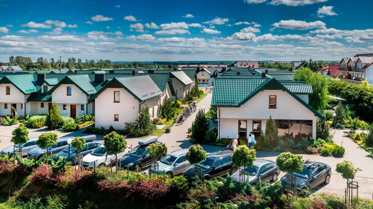 Domki apartamentowe Fulay Premium z zielonymi dachami, otoczone zielenią, z zaparkowanymi samochodami i ludźmi spacerującymi po terenie.