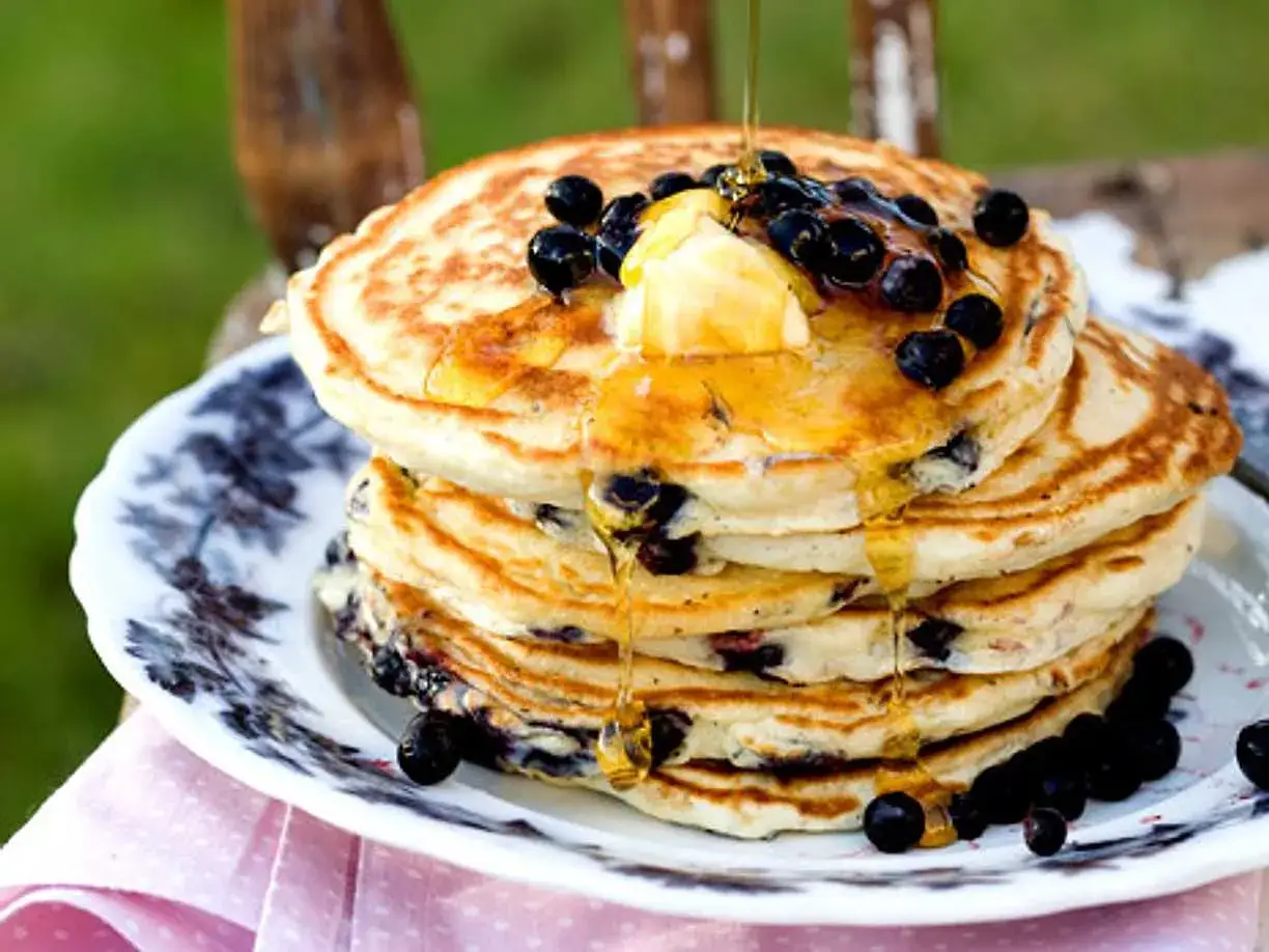 En hög med fluffiga amerikanska pannkakor, toppade med smör, blåbär och rinnande sirap. En härlig frukost!