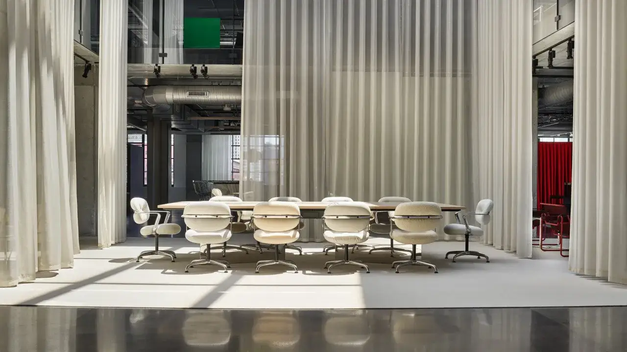 Sala riunioni moderna con tavolo e sedie, separata da tende leggere. Il passaggio minimo tra mobili garantisce fluidit&agrave;.