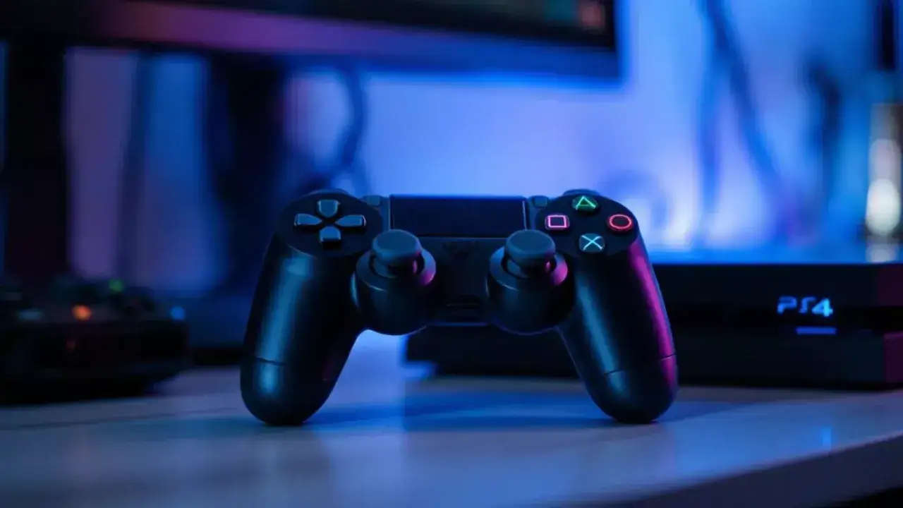 Czarny pad od PS4 na stole, w tle konsola PS4. Czy pad od PS4 pasuje do PS3?