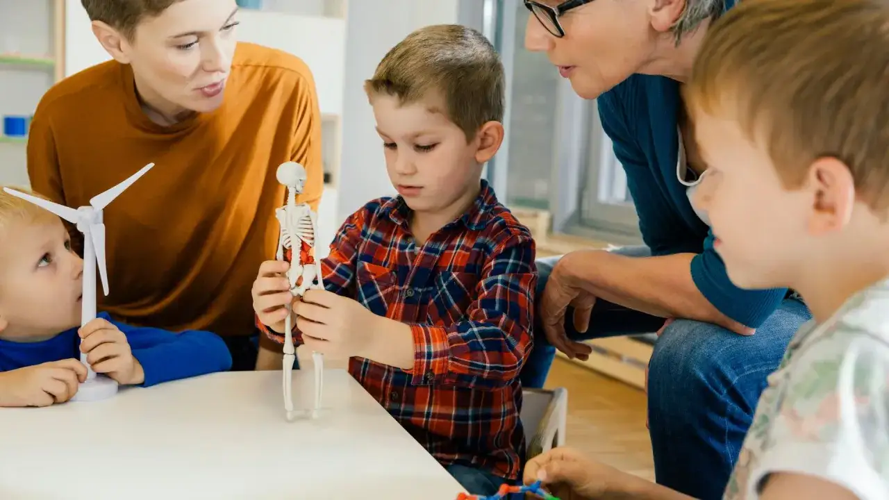 Ein Junge mit Asperger-Autismus-Spektrum untersucht konzentriert ein Skelettmodell, w&auml;hrend eine Lehrerin und andere Kinder zuschauen.