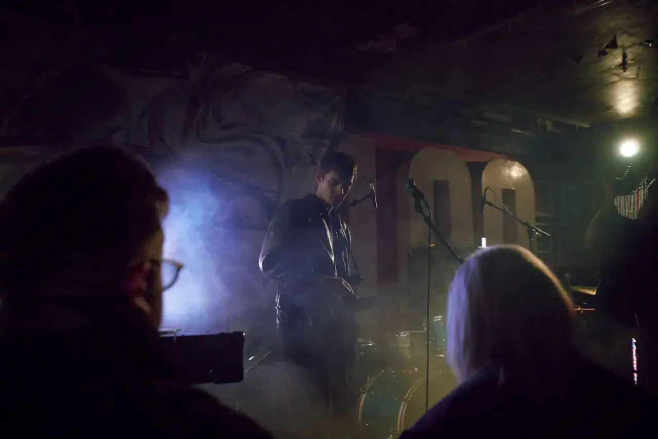 Mroczny koncert, wokalista w skórzanej kurtce, dym i światła tworzą atmosferę **goth**.