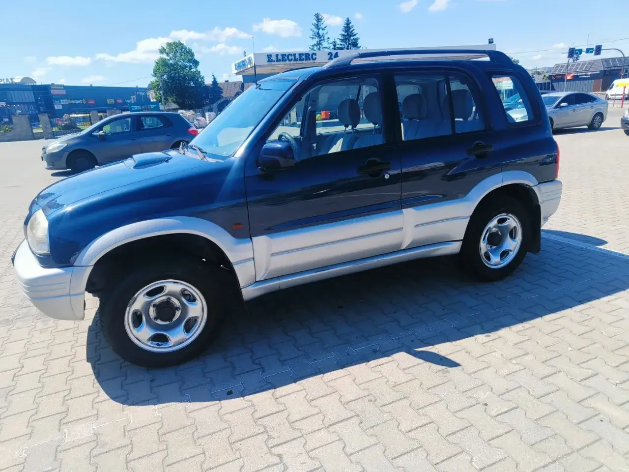 Ciemnoniebieski Suzuki Grand Vitara 1.9 DDIS z dwukolorowym nadwoziem stoi na parkingu.