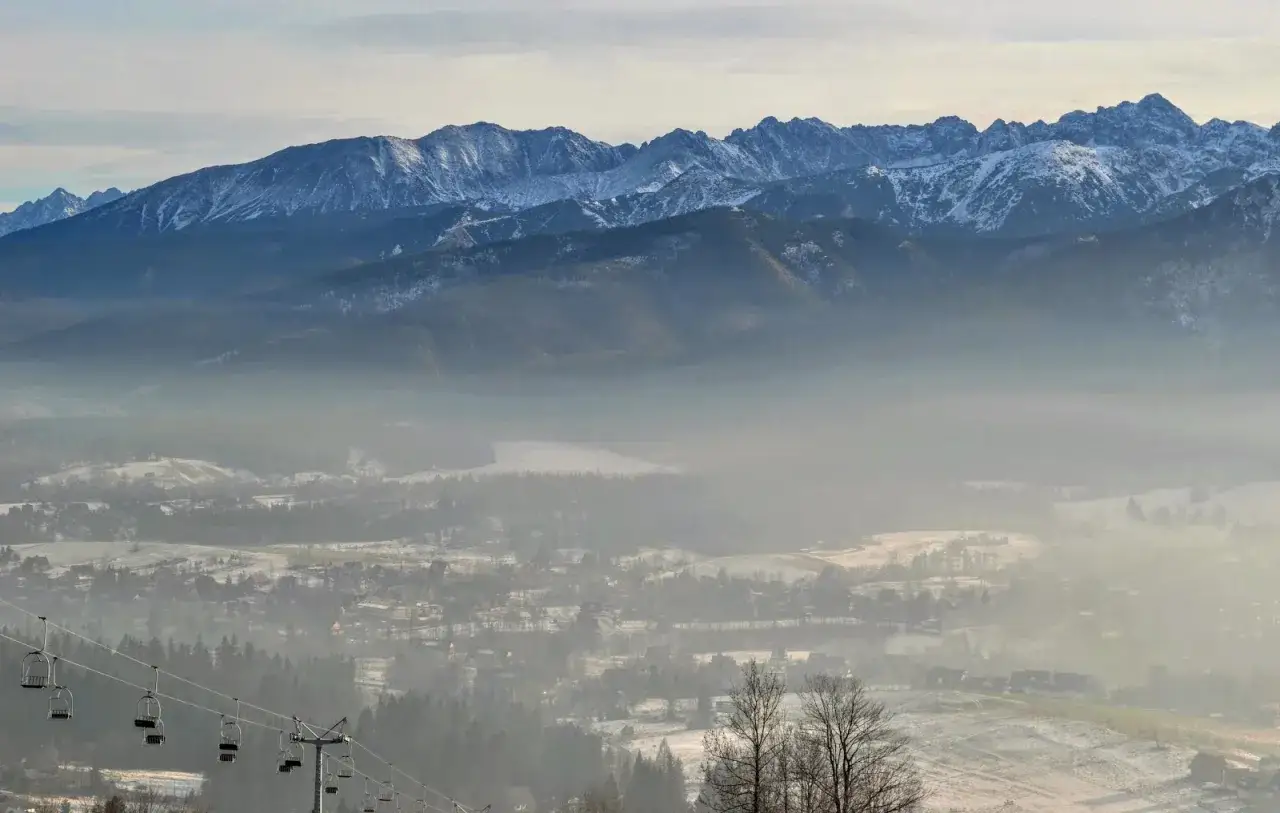 Widok na Tatry z Gubałówki. Kolejka krzesełkowa w dole, mgła nad doliną, zimowe atrakcje czekają.