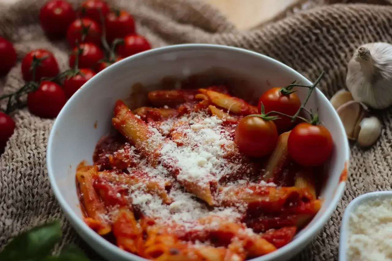 Penne z prostym sosem do spaghetti, posypane parmezanem. Obok świeże pomidorki i czosnek.