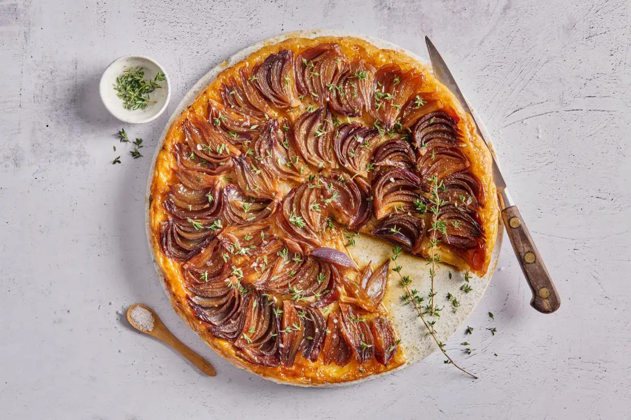 Eine k&ouml;stliche, herzhafte Tarte Tatin mit karamellisierten roten Zwiebeln und frischem Thymian, bereit zum Servieren.