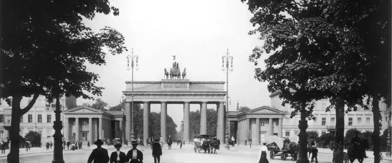 Das Brandenburger Tor, ein Wahrzeichen von historischen Orten in Berlin, mit Pferdekutschen und Menschen auf der Stra&szlig;e.