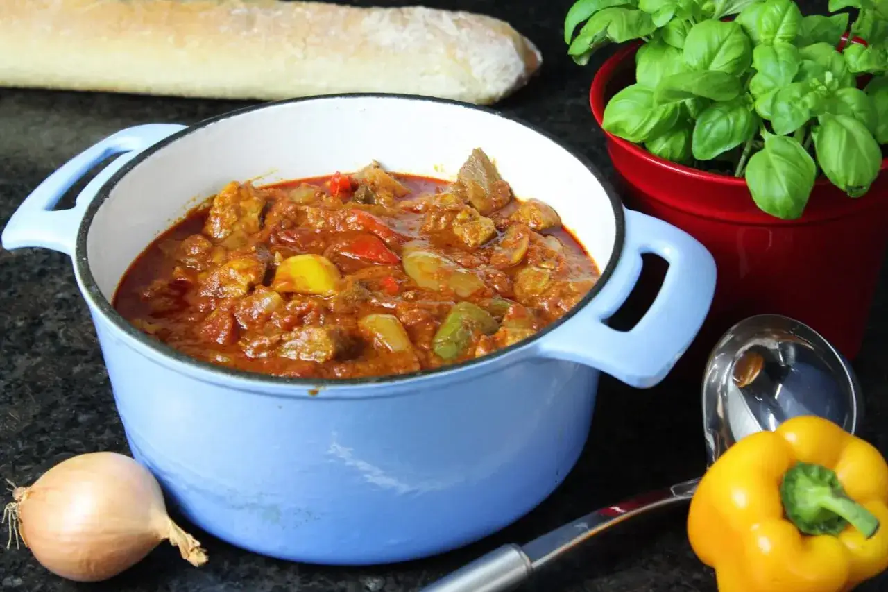 Herzhaftes Schaschliktopf Rezept in einem blauen Topf, mit Paprika, Zwiebeln und Fleisch. Dazu Baguette und frisches Basilikum.