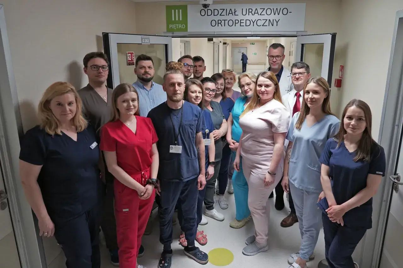 Grupa lekarzy i pielęgniarek w uniformach stoi przed drzwiami oddziału urazowo-ortopedycznego.