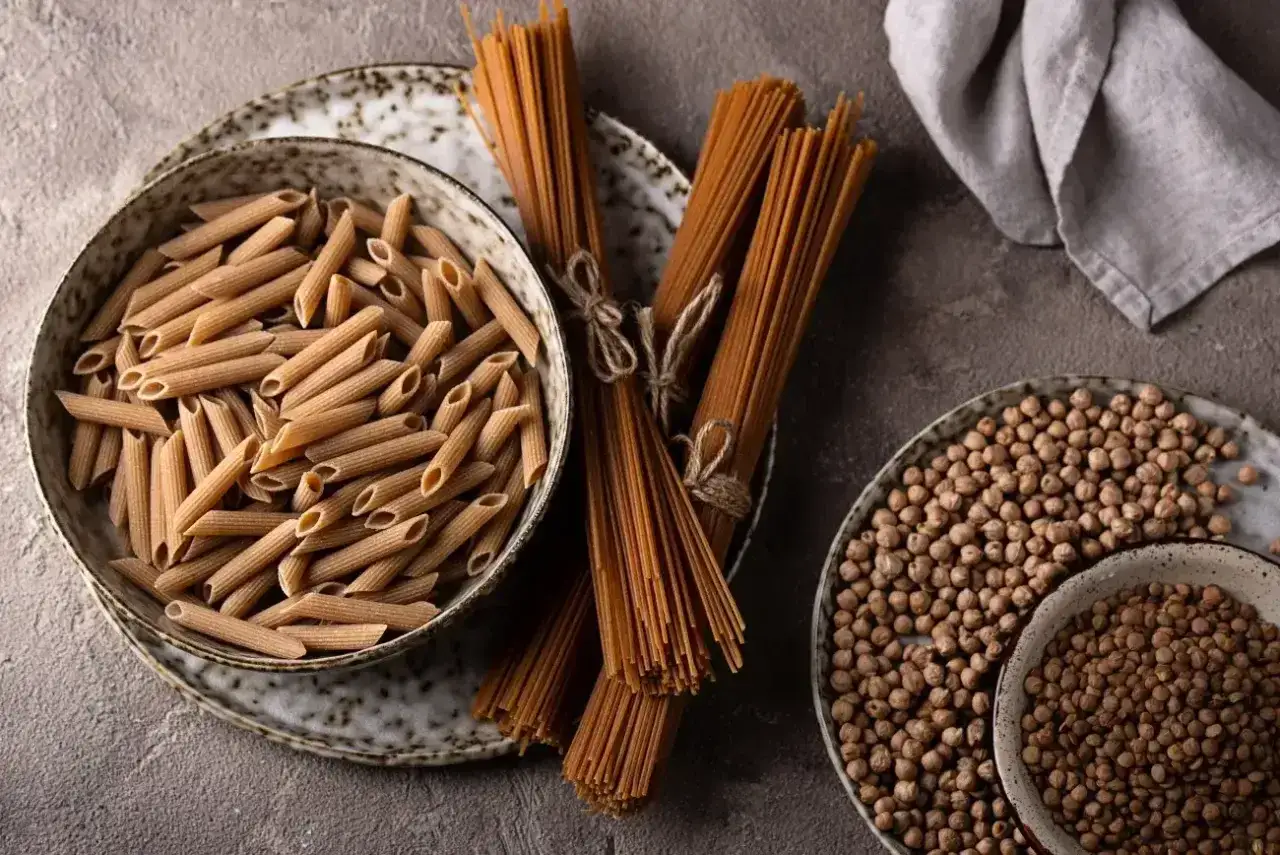 Pełnoziarnisty makaron penne i spaghetti, obok ciecierzycy. Zastanawiasz się, ile białka ma makaron? Te produkty to świetne źr&oacute;dło!