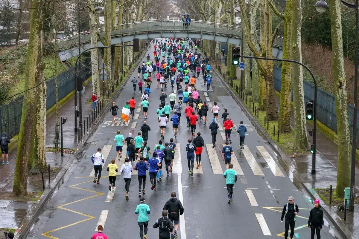 L&auml;ufer beim **Semi de Paris** auf einer von B&auml;umen ges&auml;umten Stra&szlig;e unter einer Fu&szlig;g&auml;ngerbr&uuml;cke.