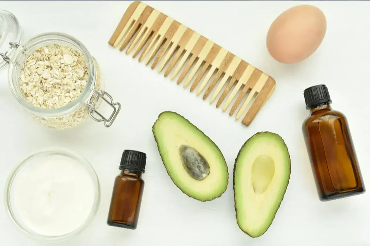 Ingredienser för hårvård: havre, avokado, ägg, kräm, kam och mörka flaskor med oljor.