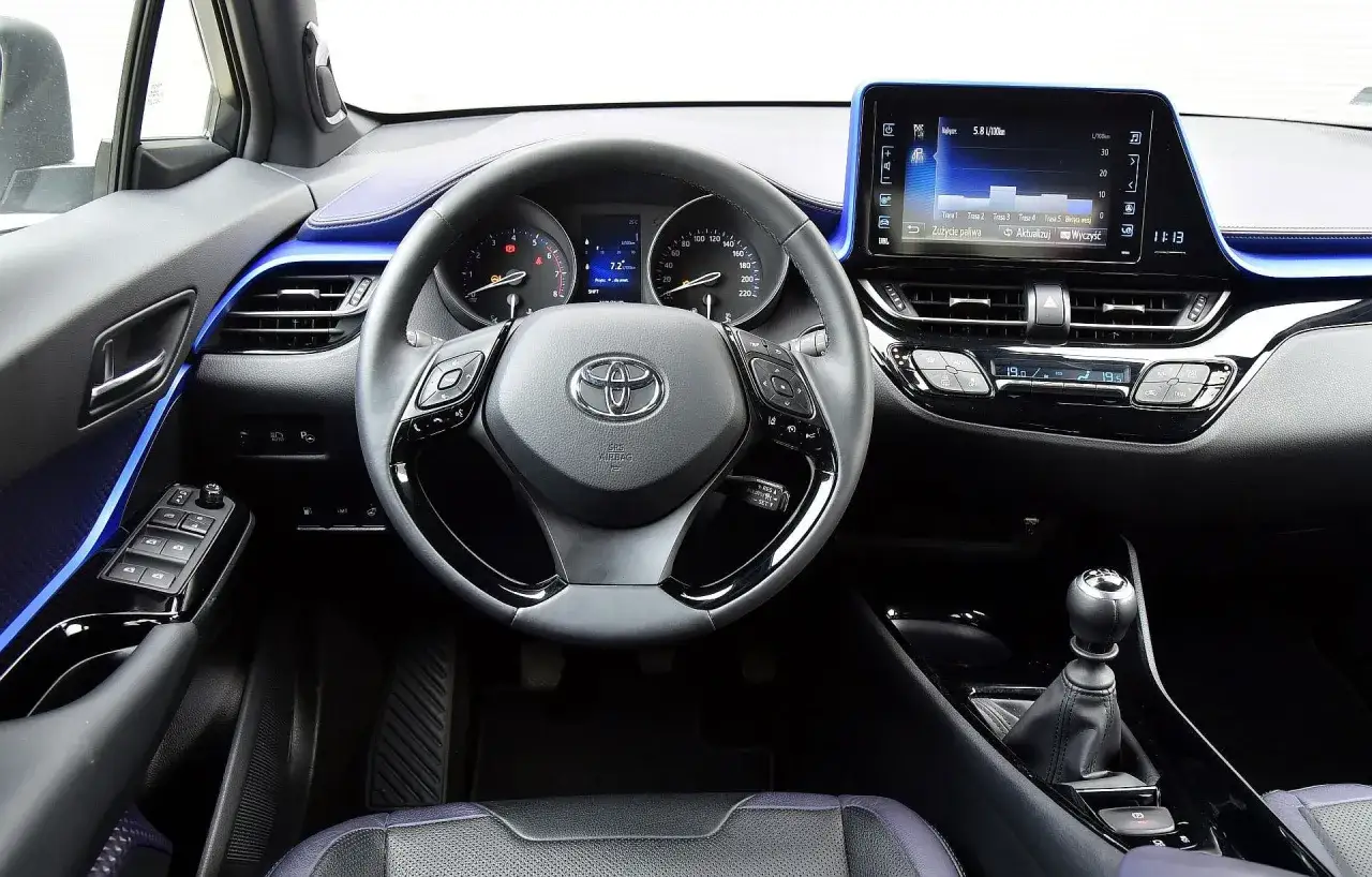 Wnętrze Toyoty C-HR 2018 z niebieskimi akcentami. Widoczna kierownica, deska rozdzielcza z ekranem multimediów i panelem klimatyzacji.