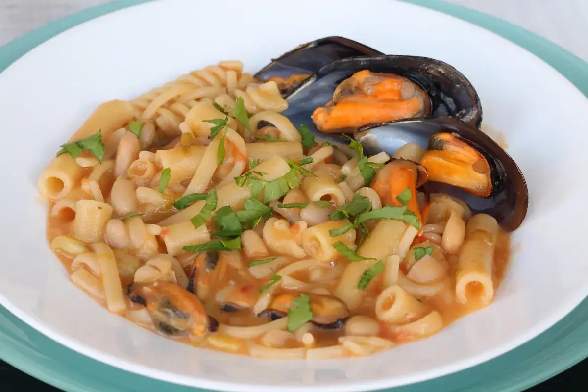 Piatto di pasta fagioli e cozze, con pasta corta, fagioli bianchi e cozze nere, guarnito con prezzemolo fresco.