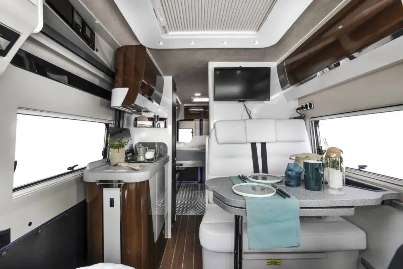 Interior de autocaravana con cocina, mesa y asientos. El dise&ntilde;o aprovecha el gran volumen para crear un espacio acogedor y funcional.