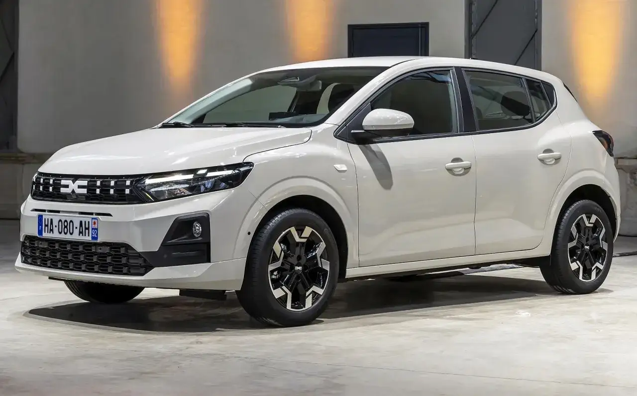 Biały Dacia Sandero na tle ściany z pomarańczowym oświetleniem. Sprawdź aktualne dacia sandero - ceny i dostępne wersje.