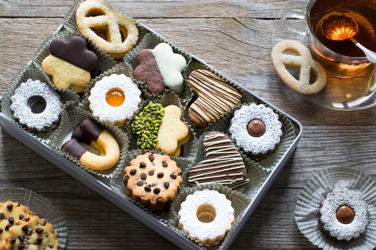 Scatola piena di biscotti di pasta frolla decorati: a forma di cuore, con cioccolato, marmellata e pistacchi.