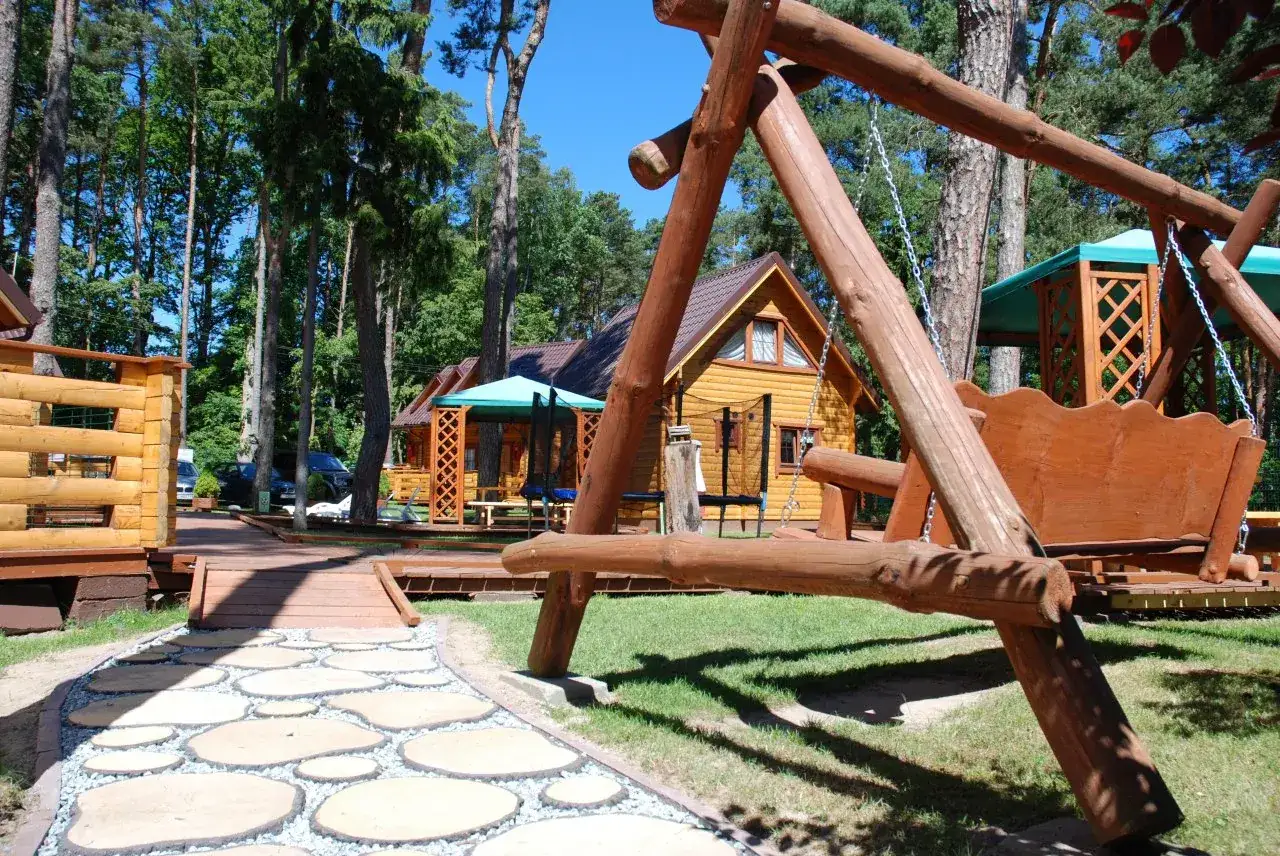 NawaroPark Pobierowo domki letniskowe: drewniana huśtawka i ścieżka z kamieni prowadzą do urokliwych domków w otoczeniu lasu.