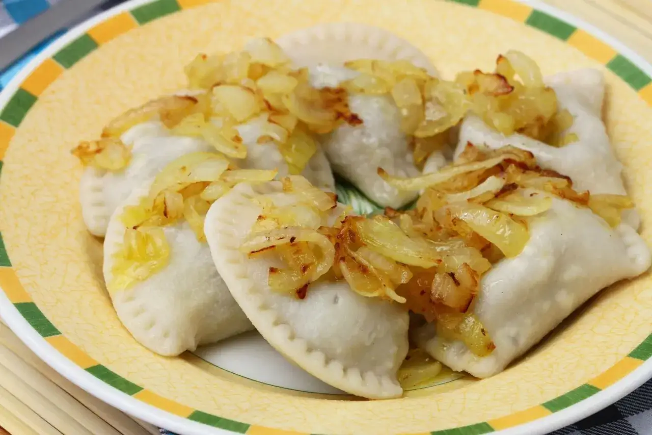Pyszne pierogi, które przypominają o tym, skąd pochodzą. Podane z podsmażoną cebulką na żółtym talerzu.